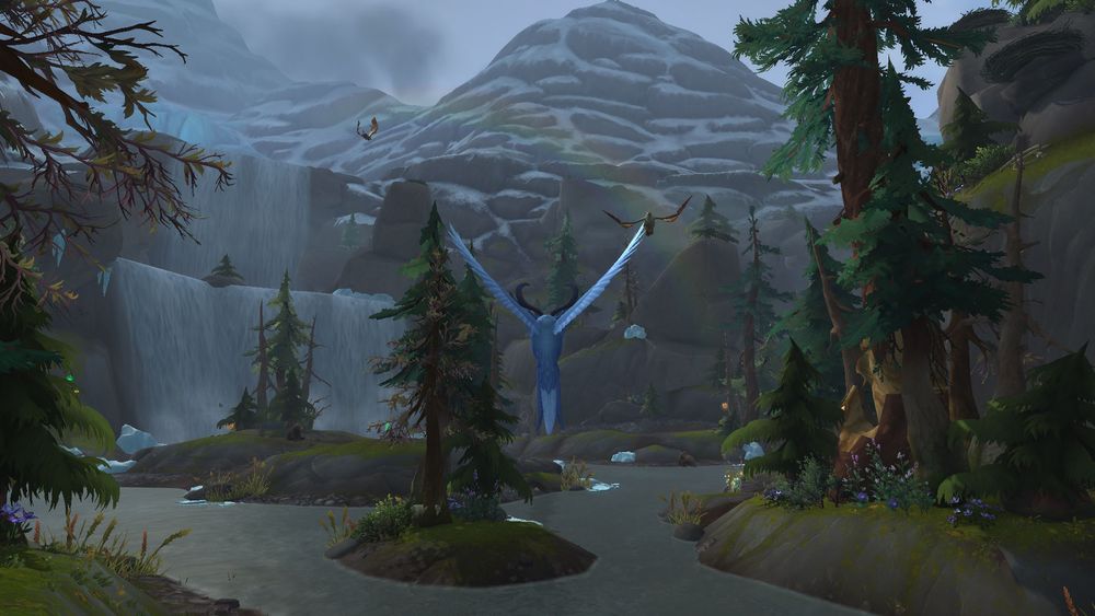 A druid in their flight form, the pale blue somnowl from Dragonflight, hovering above a river in Boralus. A two-tiered waterfall feeds the river in the background, and even further back, snow-capped mountains take up the sky. Above the river, a pair of griffins fly through the arch of a rainbow.