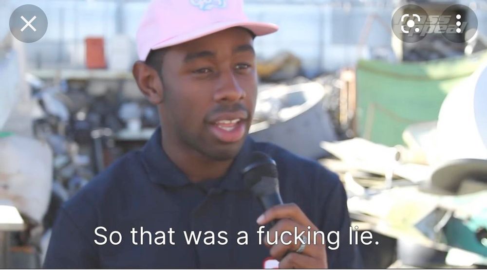 picture of tyler the creator wearing a dark blue polo and a baby pink baseball cap. he's holding a microphone. across the image is the sentence, "so that was a fucking lie."