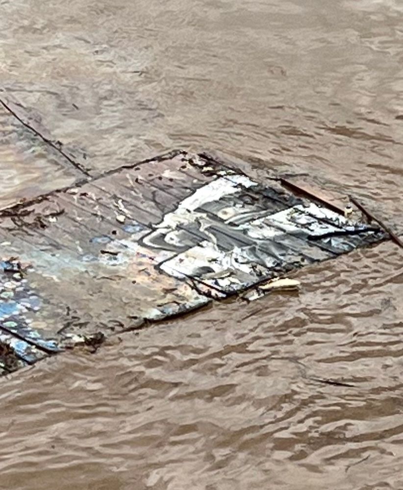 Cartoonish graffiti skull on wooden wall ripped from floodwaters floating in oily sheen 