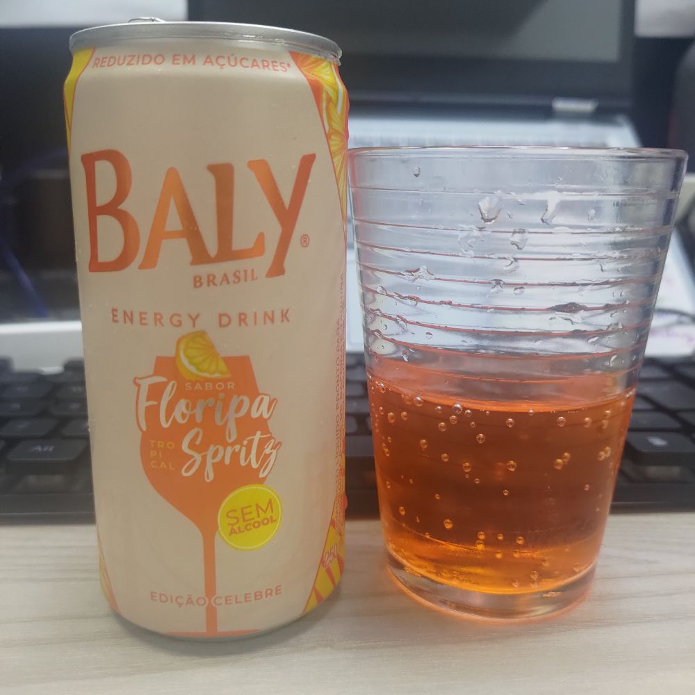 Lata de Baly 250ml, sabor Floripa Spritz, e um copo com um líquido tipo refrigerante bem laranja forte e escuro.
