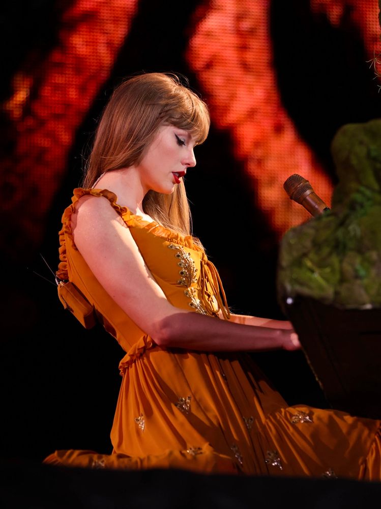 taylor swift on stage at the eras tour, playing the piano and performing champagne problems