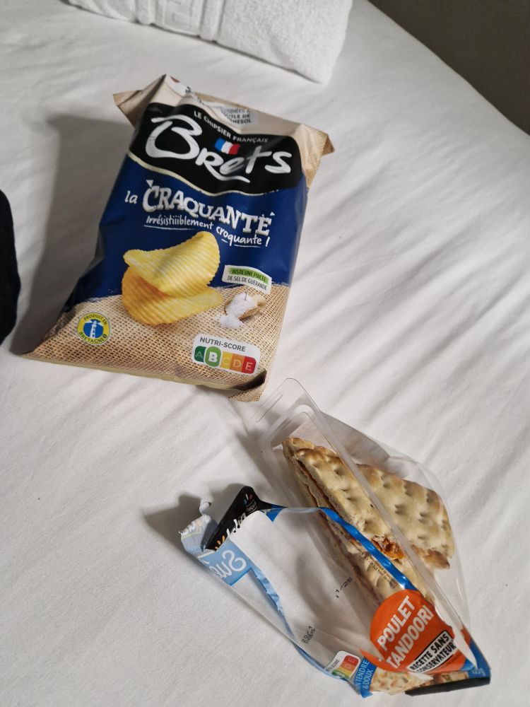 A wrapped tandoori chicken sandwich and some French crisps laid out on a bedsheet. The vibe is unimpressive. 