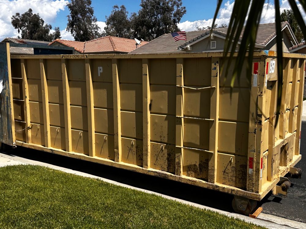 Picture of a mustard yellow 30 cubic yard metal dumpster parked on the street in a Southern California neighborhood.