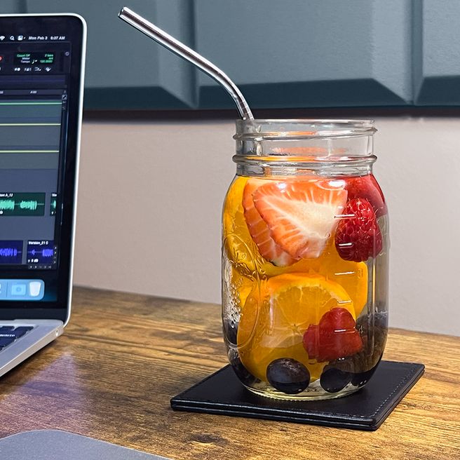 A Mason jar filled with berry-infused water sits beside a laptop on a wooden desk, creating a vibrant and inviting workspace.