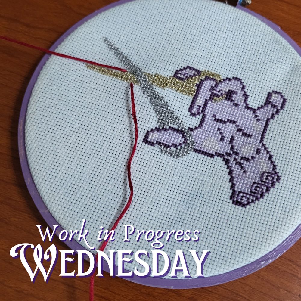 A cross stitch project finished in an embroidery hoop showing a hand holding a pair of scissors, stitched in silver and gold metallic threads.  On the wrist are backstitch details in greek motifs.  A long, red string is weaved into the project to look like the scissors are snipping them. Work in Progress Wednesday.
