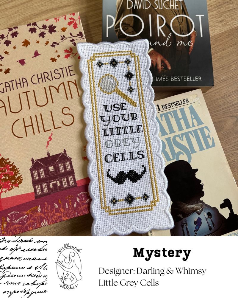 Staged on Agatha Christie novels, this scalloped-edge bookmark shows small diamond motifs, a magnifying glass, and a giant mustache.  Backstitched text says “Use Your Little Grey Cells." Spellbound Stitches logo.  Mystery.  Designer Darling & Whimsy. Little Grey Cells.