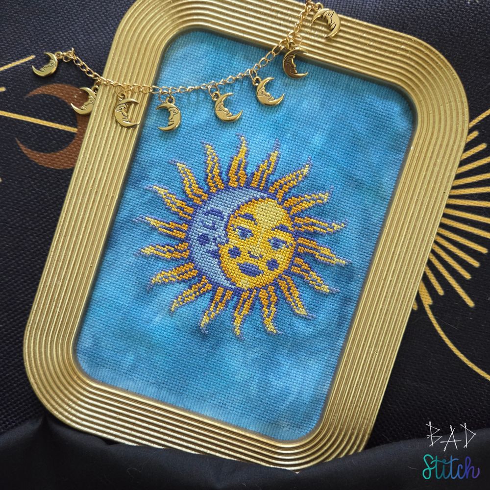 A gold framed cross stitch project showing a retro sun and moon motif. BAD Stitch.
