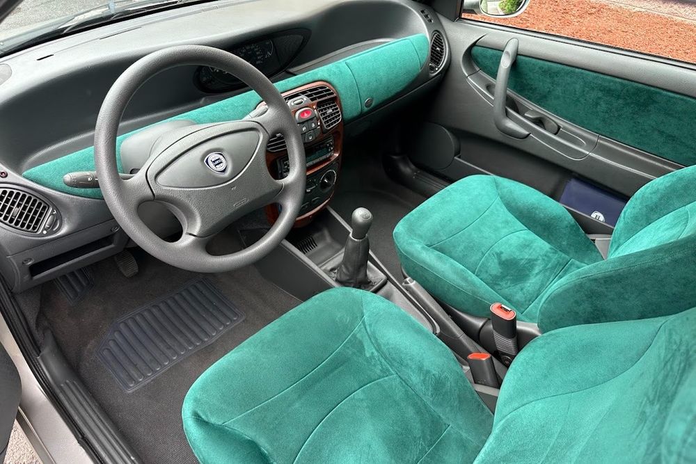 Interior of a Lancia Y, a combination of gray plastics, extremely teal cloth seats and dashboard, and wood-grain trim.
