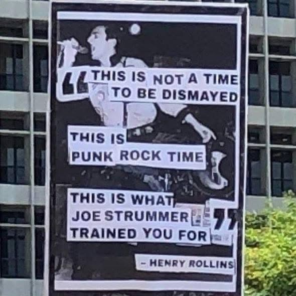 A protest poster with a photo of a fired up Joe Strummer at a microphone. Overlaid is a quote from Henry Rollins: “This is not a time to be dismayed. This is punk rock time. This is what Joe Strummer trained you for.”