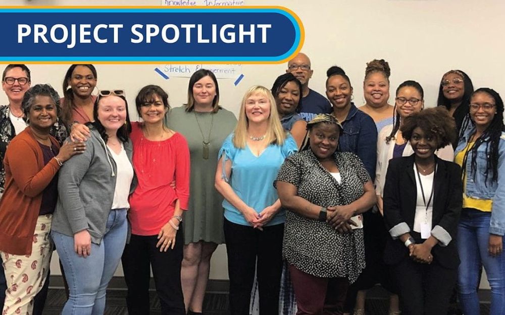 A group of 16 people are standing together and smiling into the camera. A dark blue banner that says "project spotlight" goes across the top left part of the image.