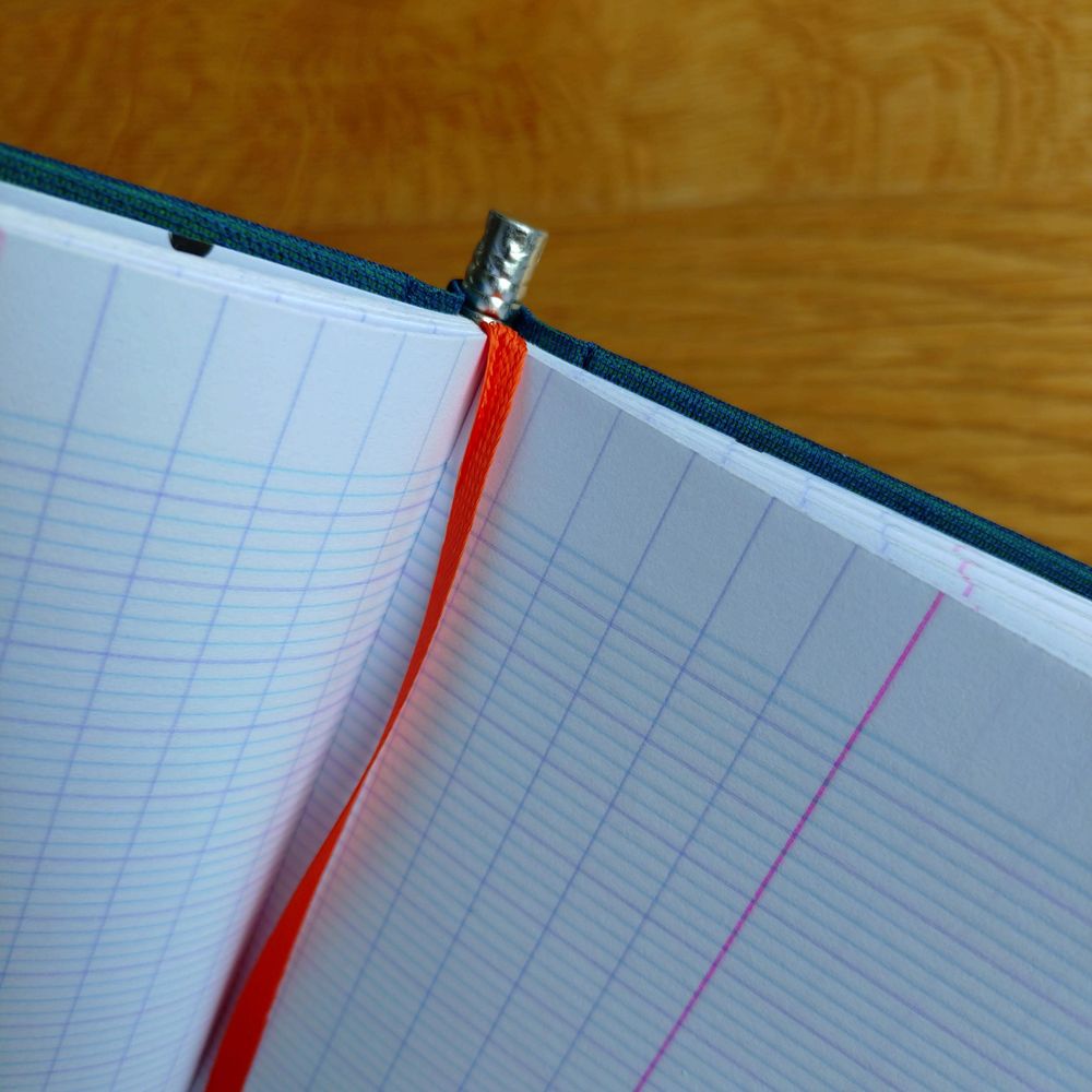 detailansicht des innenlebens des notizbuches: der im rückensteckende bleistift, das linierte papier und ein orangenes lesezeichenband