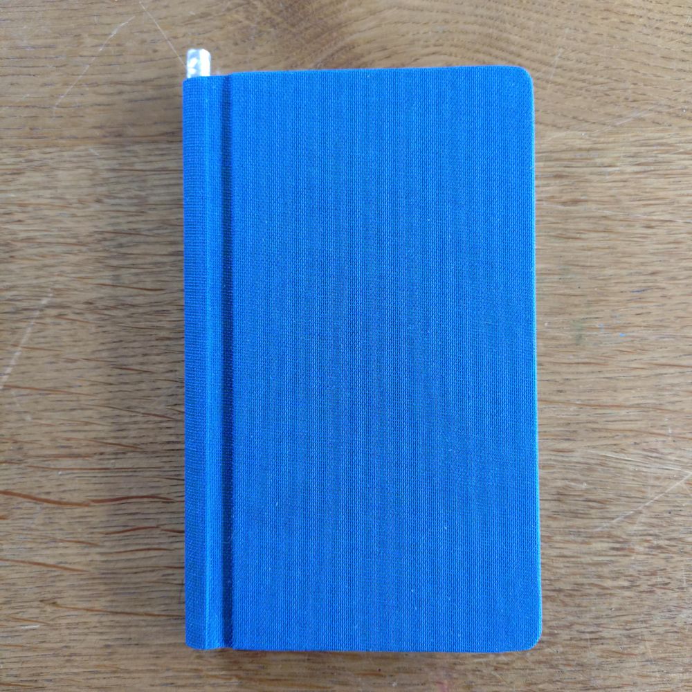 foto eines ca. A6-großen blauen notizbuches; der einbandstoff hat einen grünschimmer, den mein handy in der von-oben-ansicht nicht eingefangen bekommt