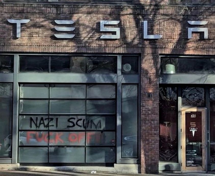 Graffiti on Tesla storefront reading, "Nazi Scum, Fuck Off!"