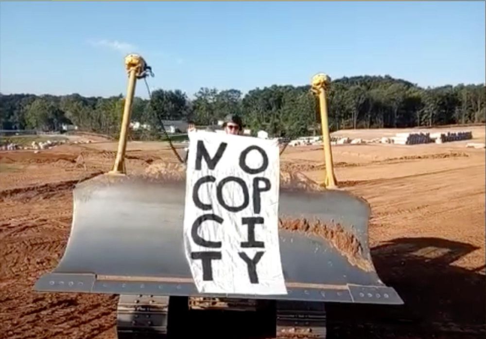 Protester holds, "NO COP CITY" banner while on bulldozer.