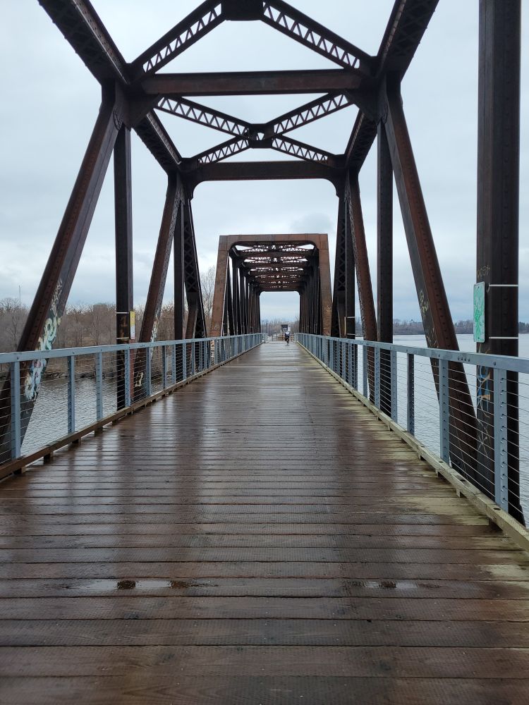 Wooden bridge stretching away with river underneath. 
