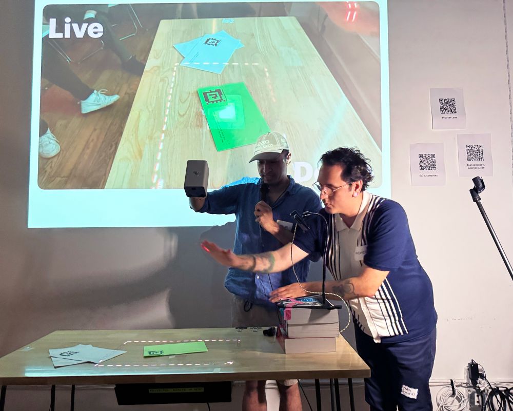 Omar and Andres demonstrating the folk Gadget by projecting light onto pieces of paper with code and tags printed on it.
