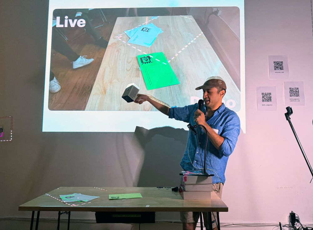 Omar demonstrating the folk Gadget by aiming a triggered, handheld device and projecting light onto pieces of paper with code and tags printed on it.