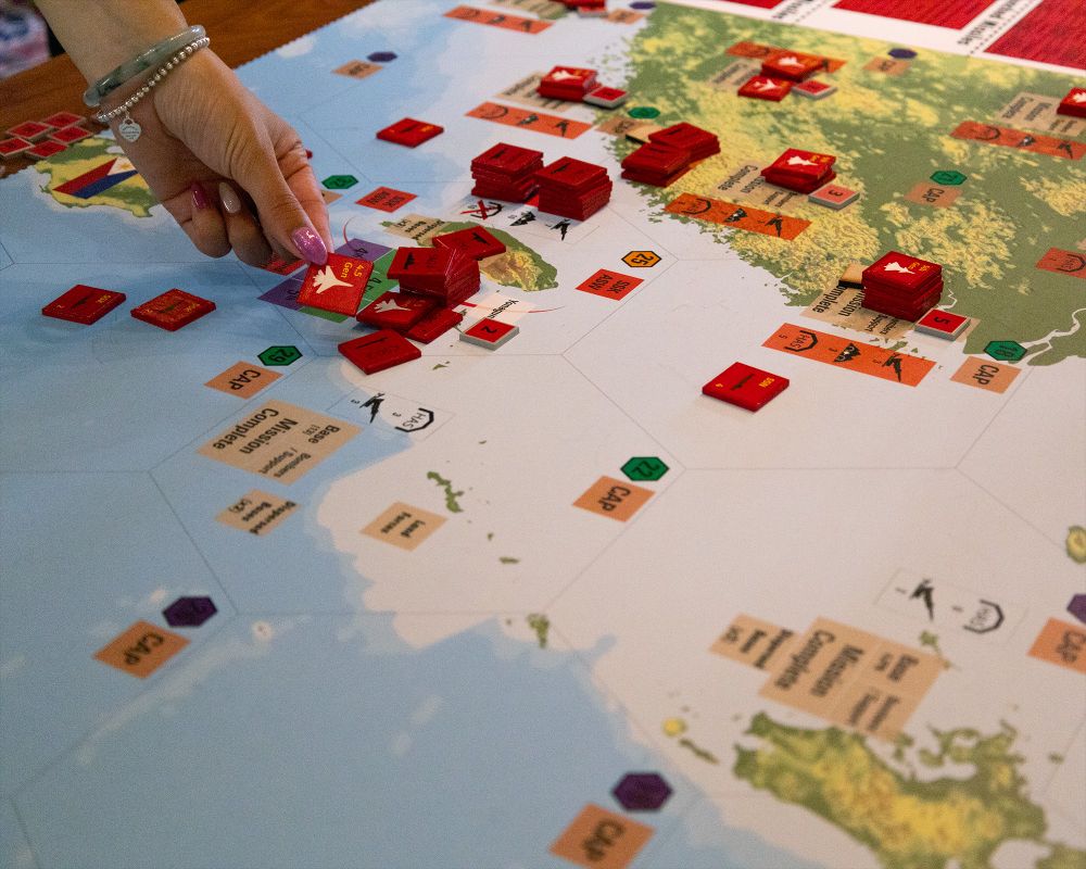 A hand places a tile on a game board.