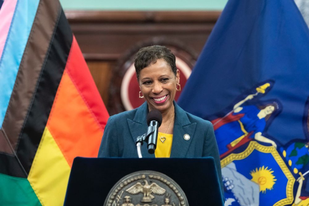 Council Speaker Adams at the lectern with an LGBT flag and a NY flag in the background.