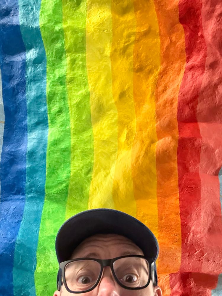A selfie (from the nose up) in front of a rainbow. 