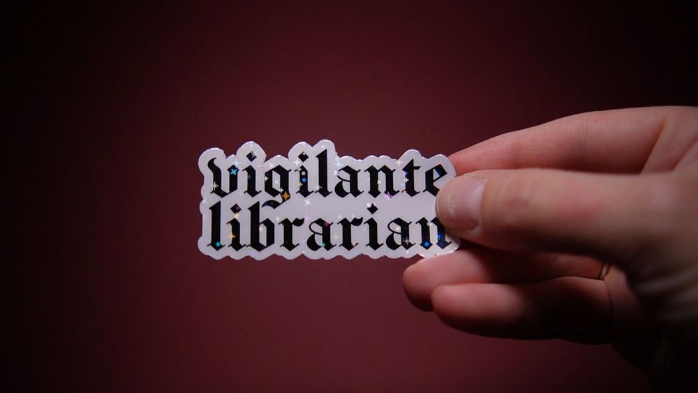 A sparkly vinyl sticker reading “vigilante librarian” in blackletter font