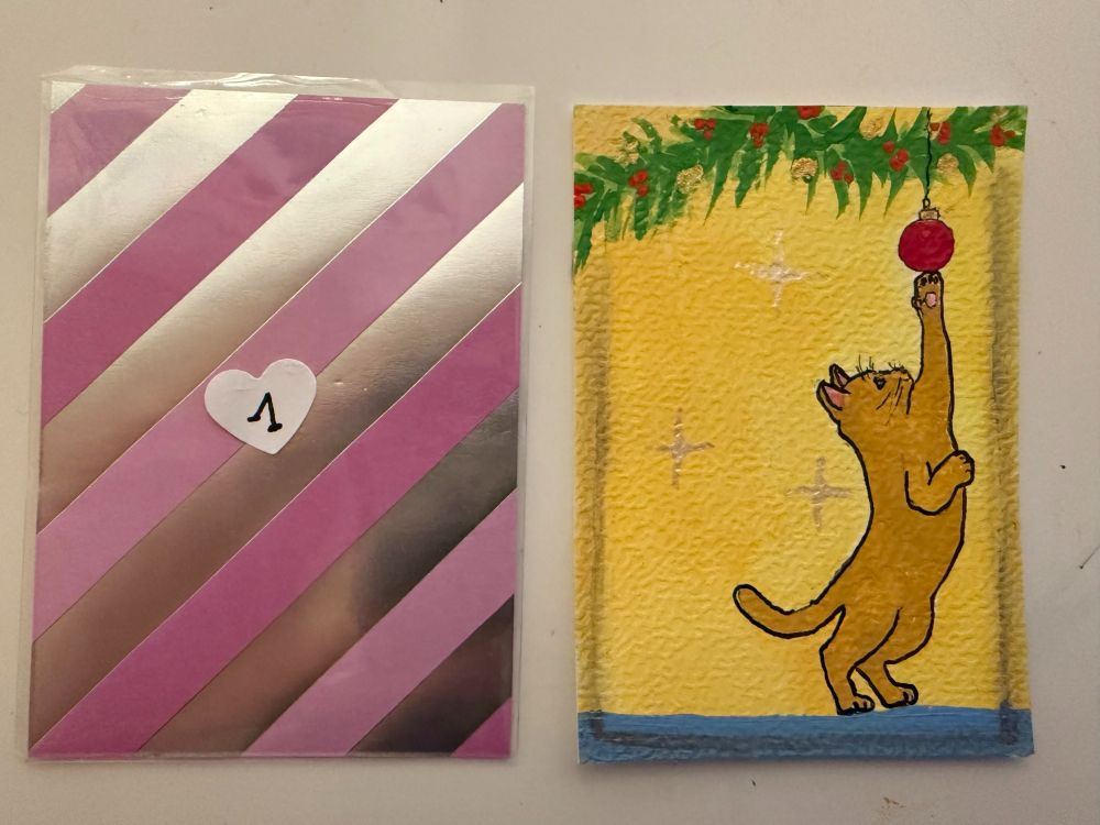 Artist Trading Card mit einer Katze auf den Hinterbeinen, welche nach einer Weihnachtskugel greift. Die Kugel ist an einem Tannenzweig befestigt. Gelber Hintergrund mit funkelnden Sternen.