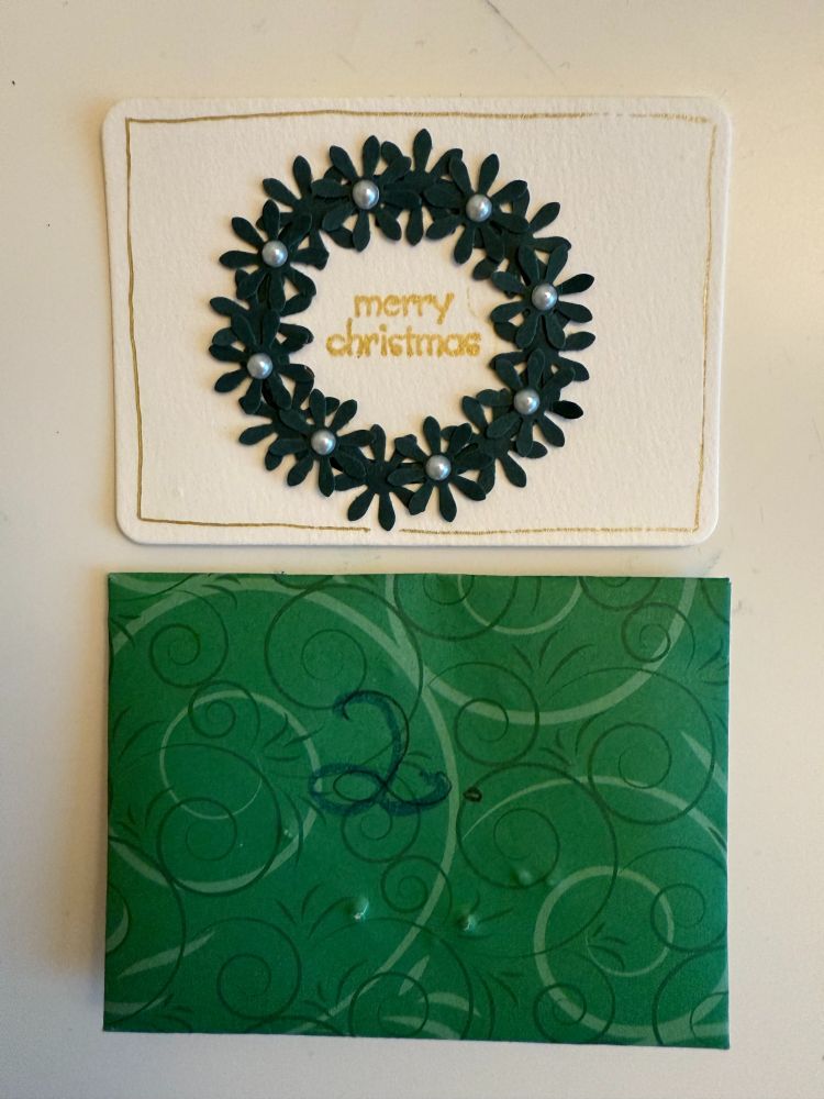 Artist Trading Card mit einem Weihnachtskranz. Kranz ist gebaut aus aufgeklebten, grünen Blumenteilen und kleinen Perlen. Schriftzug "Merry Christmas" in Gold in der Mitte.