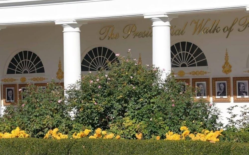 The covered White House colonnade running to the West Wing. Portraits of past presidents line the walkway and it has been decorated with breathtakingly tacky gold ornaments included the words "The Presidential Walk of Fame" in huge letters above the arched mullioned windows.