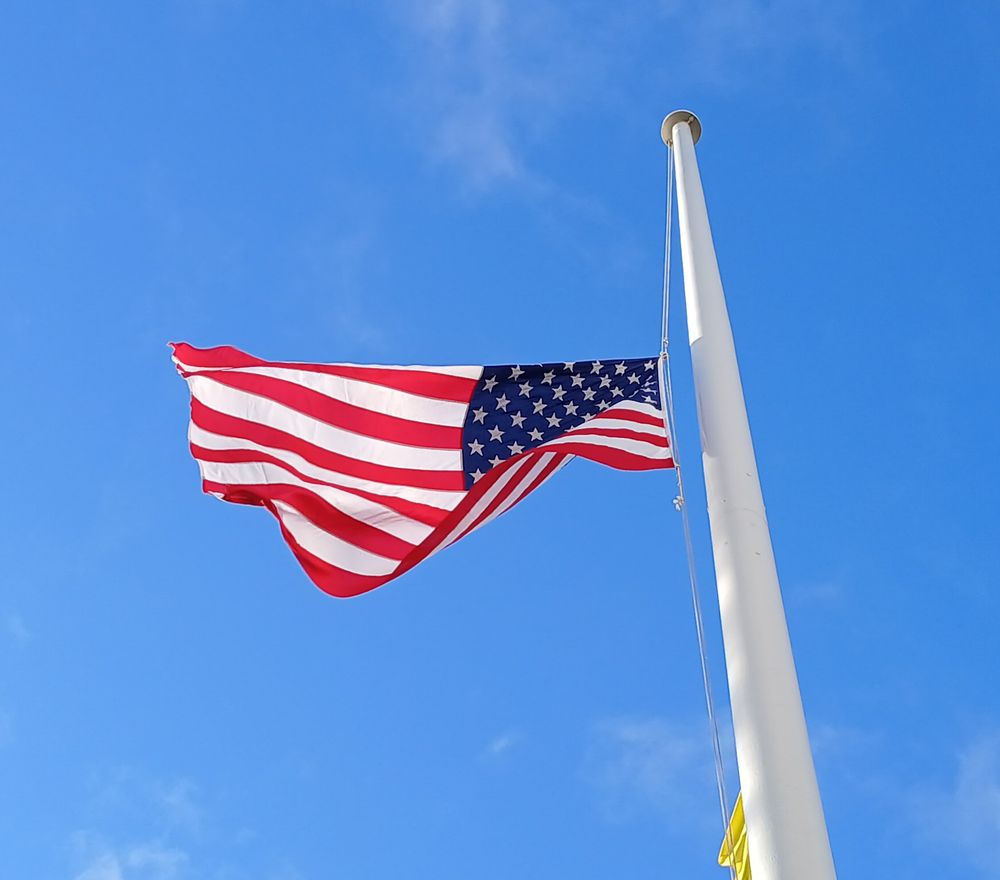 The US flag at half mast against a blue sky.