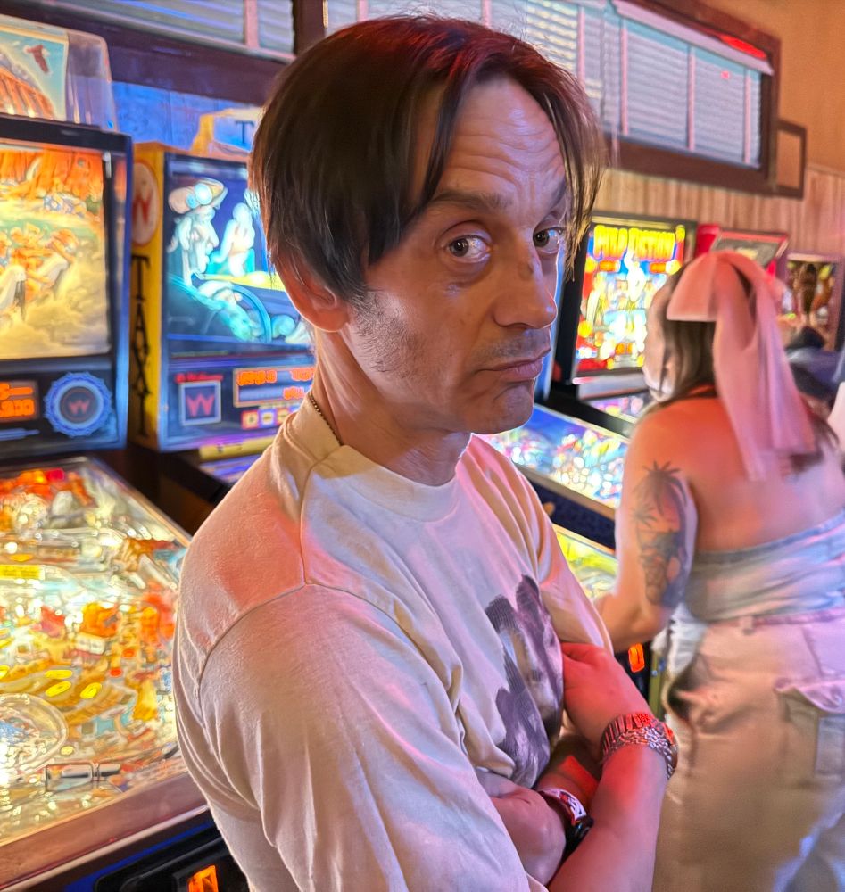Portrait of Danny Backglass in front of pinball machines.