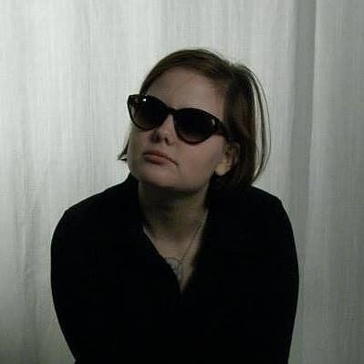 A photo portrait of the author of this skeet when she was 22. She is in a black dress and is wearing sunglasses and long brown hair.