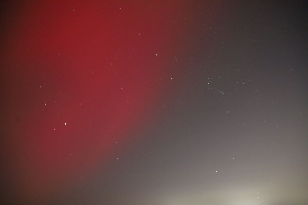 Two photos of a similar scene. Toward the center are the stars that make up the constellation orion, a polygon with a belt of three stars. In this photo, a wave of scarlet aurora sky seems to stretch to orion from the top left. 
