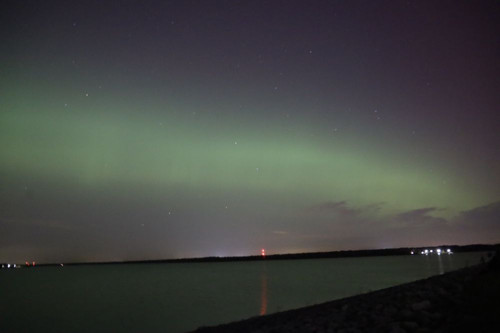A green soft aurora arc shoots across the sky, reflecting in a cold gray lake below. 

