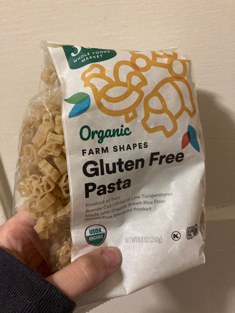 Hand holding a small bag of organic gluten free pasta from Whole Foods in small shapes like chickens and tractors