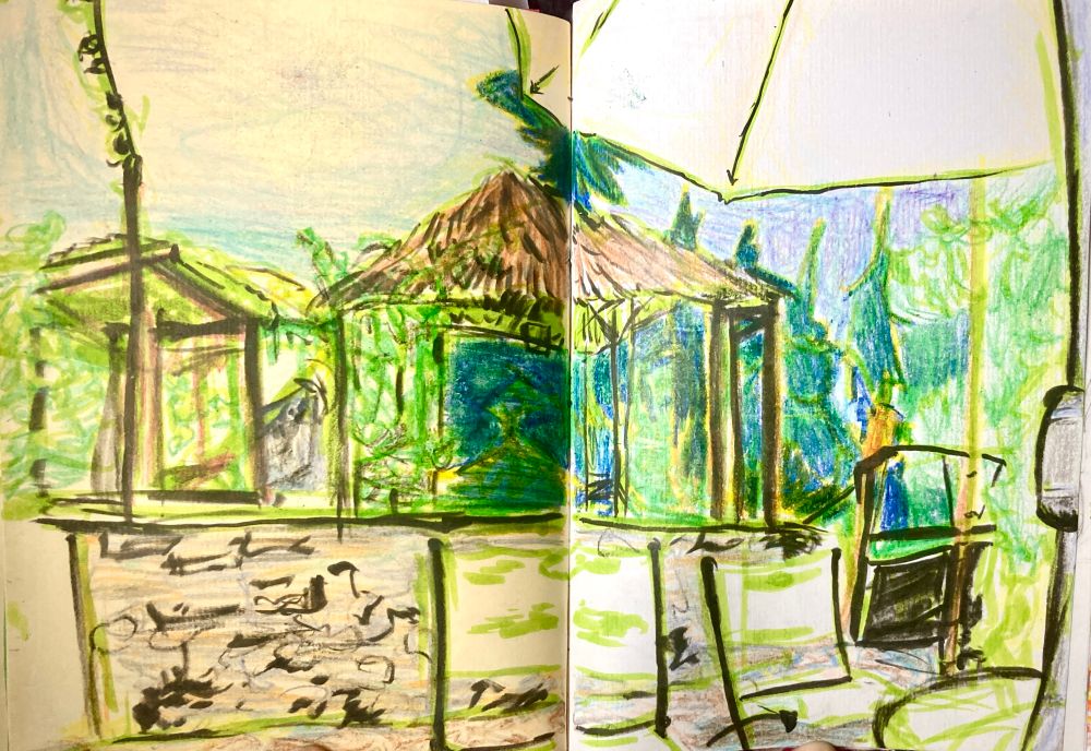 nature drawing sitting on a porch under an umbrella, facing a wooden overgrown shelter with string lights.