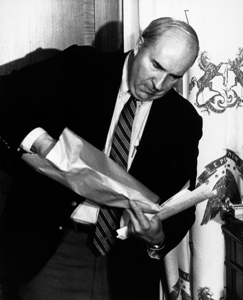 A photo of Budd Dwyer reaching into a paper bag, about to show everyone what he brought for lunch