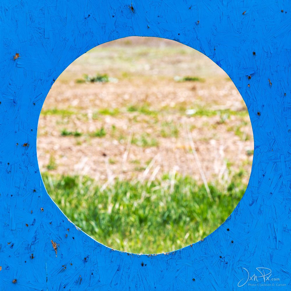 A large hole in a blue target board out in a field.