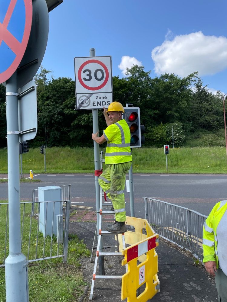 A worker in high visibility clothing installs a 30mph sign on a road in Edinburgh.  