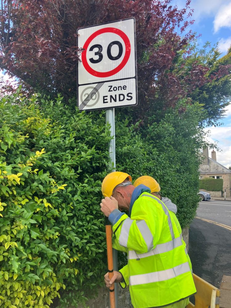 Two workers in high visibility clothing install a 30mph sign on a road in Edinburgh.  
