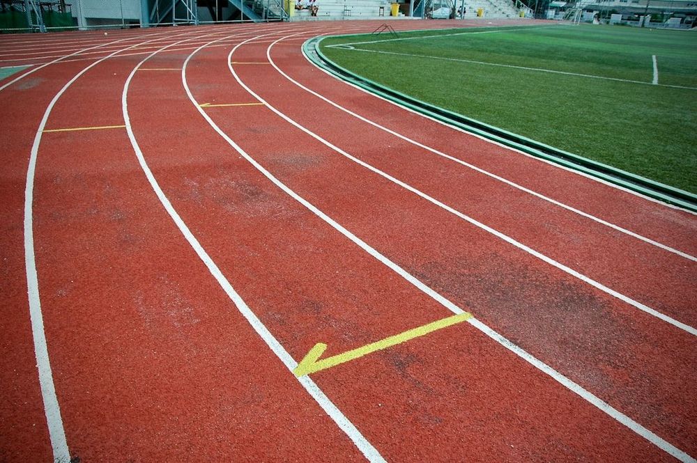A close up photo of an orange school running track with a field in the background.
