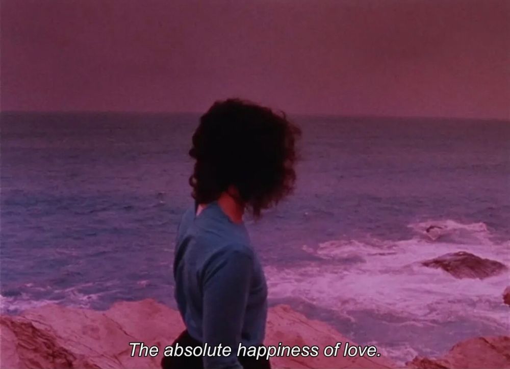 Une femme, de dos, regarde l’océan. Le ciel et la mer sont rose. 