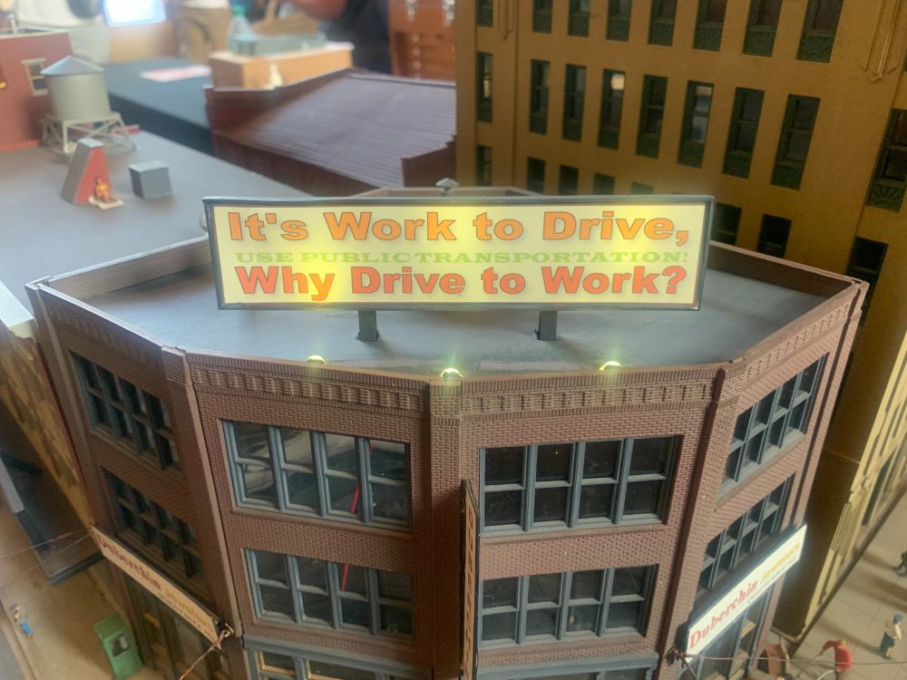 Model house with a sign that says "It's work to drive, why drive to work?"