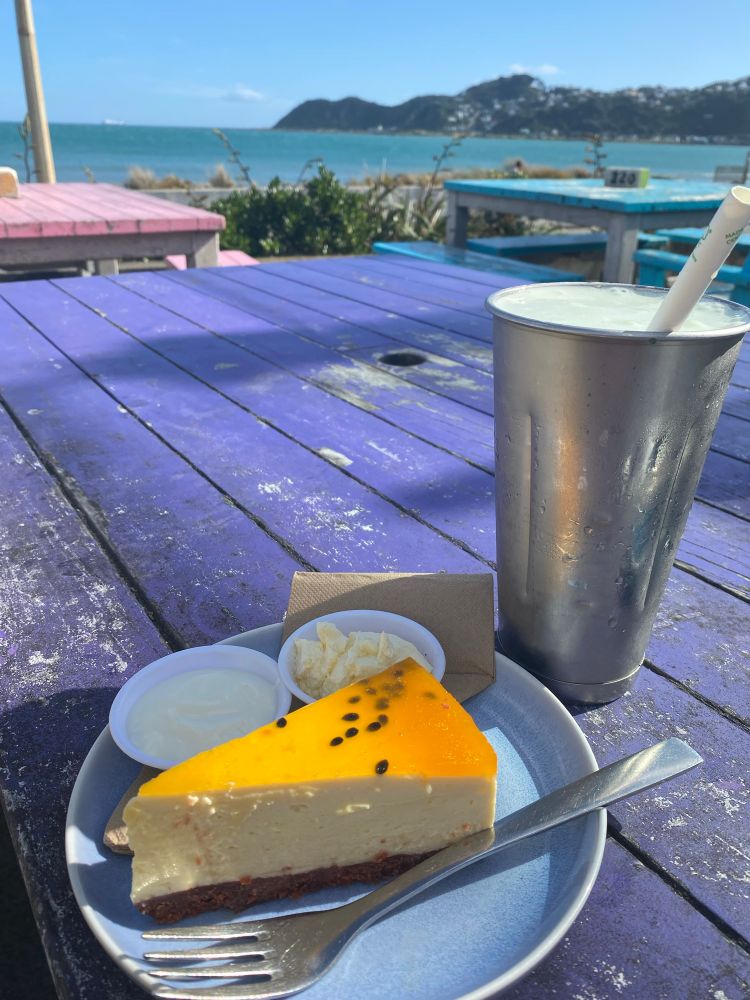 Sea view from a sunny pink table on which rests a milkshake and a passion fruit cheesecake
