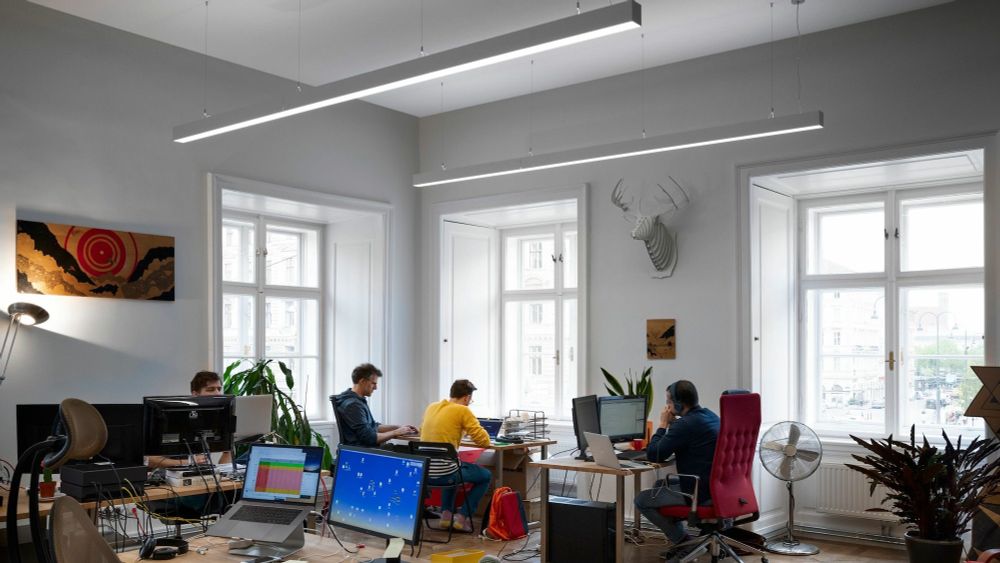 Photo showing 4 people working on computers in a high-ceiling room with 3 big windows