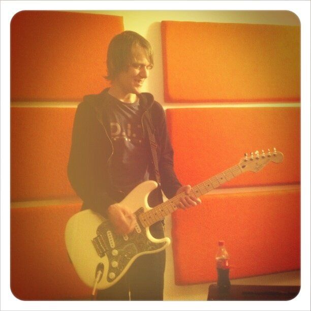 a picture of me with hair. i'm in one of the rooms in blueprint studios in salford, there's cool looking orange sound proof padding behind me, and there's a slight vintage type filter applied by the absolute poser who took it. as for me i'm wearing a black hoody unzipped and i'm playing my white mexican strat, where i took the scratch plate and sort of glued an old floral green shirt over it, which looks really cool. the fingerboard is maple. that matters because it's cool. also my hair is not long, but long ish. i'm about 25 i think.