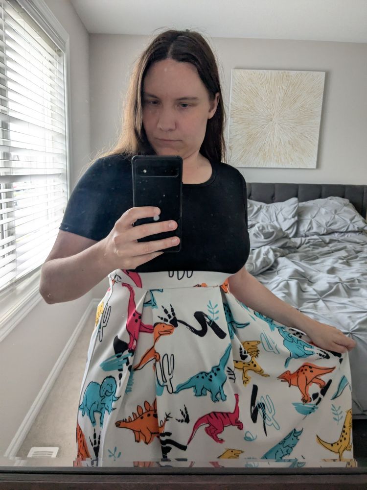 A dress with a black short sleeve top and long white skirt. The skirt is decorated with cartoon dinosaurs in bright colours.