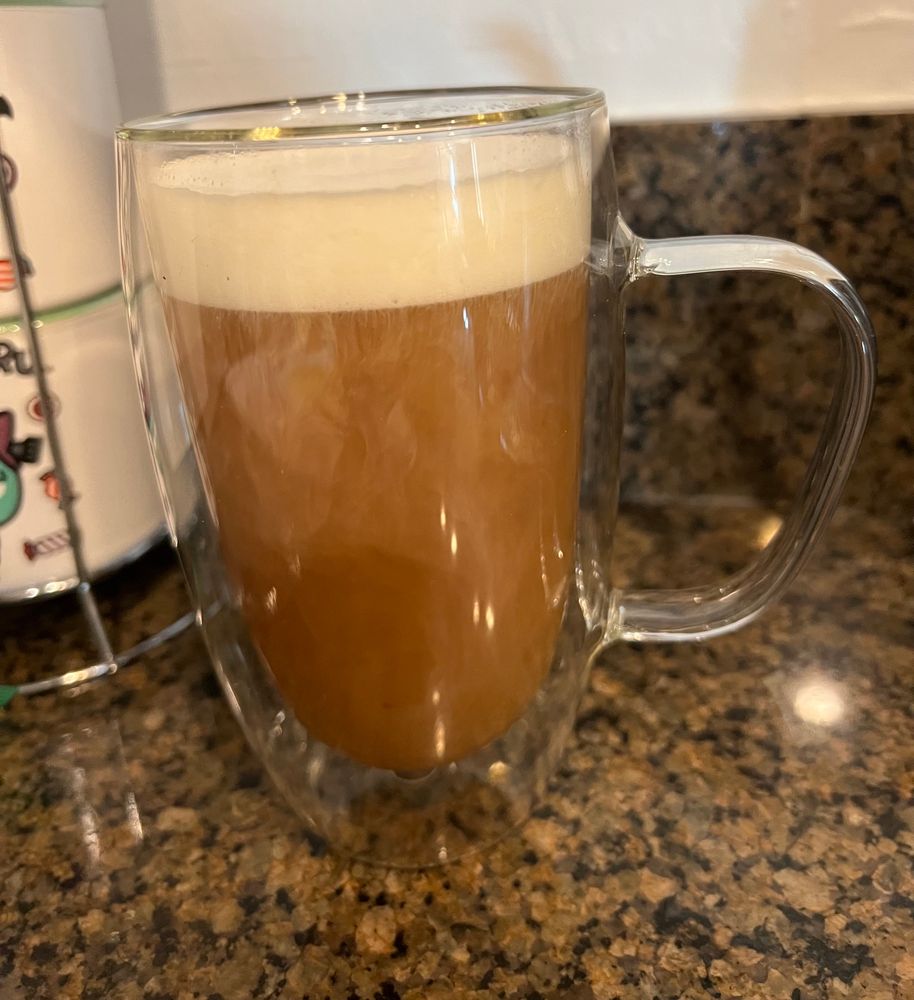 A tea latte in a double layered glass mug on a speckled countertop.