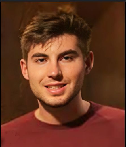 A photograph of Marco Elez. He is wearing a red t-shirt and has brown, tussled hair in this photo.