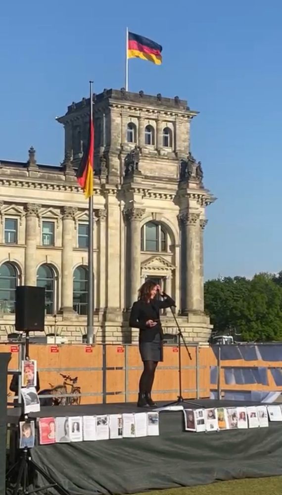 Frau Grande spricht auf dem  Podest ins Mikrofon, im Hintergrund der Reichstag