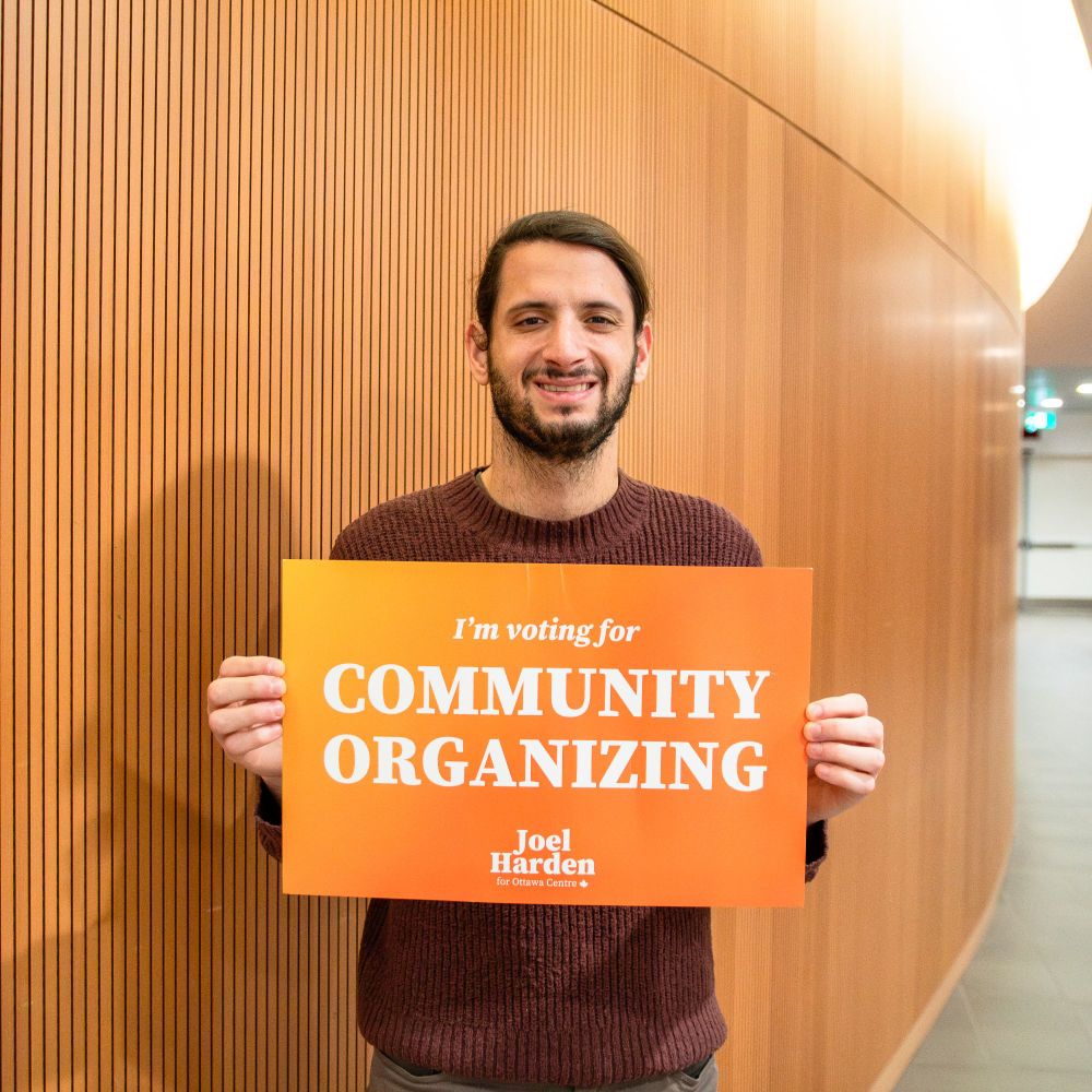 Sam Hersh holding a sign that reads "I'm voting for community organizing"